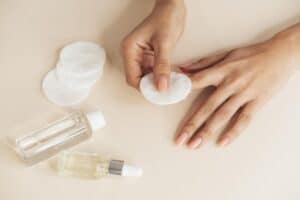 Mãos com unhas cuidadas usando algodão e produtos de manicure