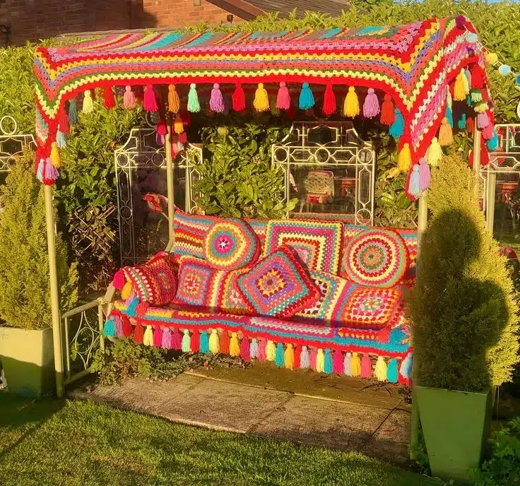 Canto de jardim decorado com crochê maximalista, com almofadas e estrutura do sofá em cores vibrantes e franjas.