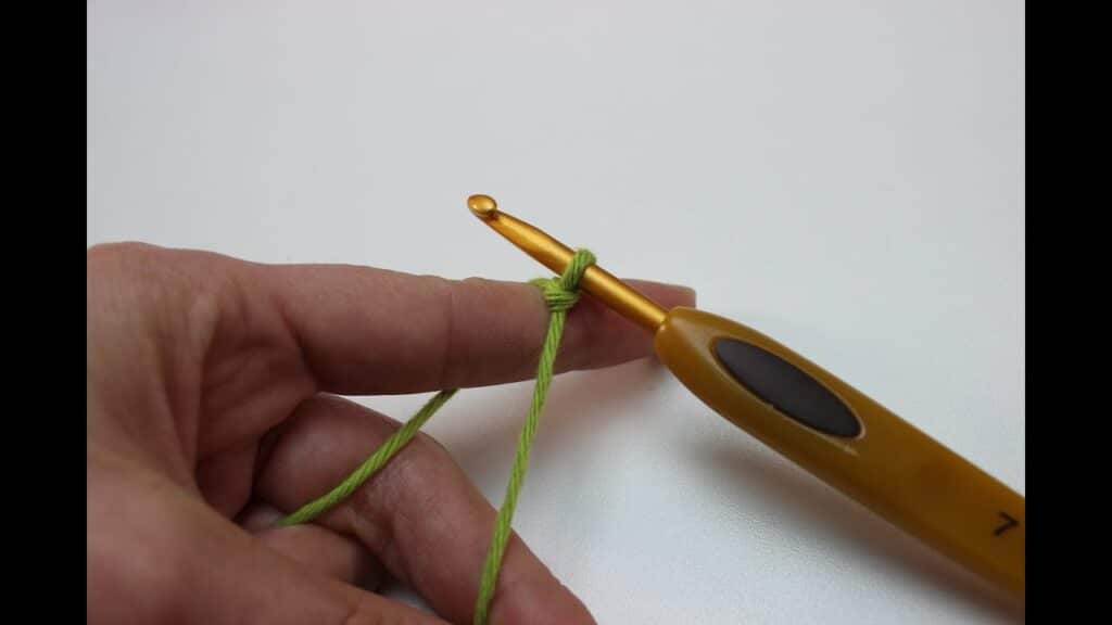 Agulha de crochê com fio verde mostrando o nó inicial