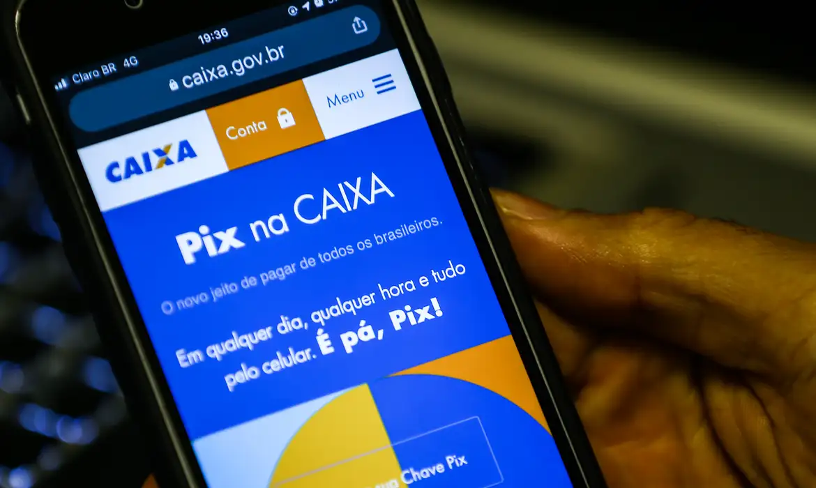 Celular mostrando site da Caixa para fazer Pix com mão de idoso ao lado