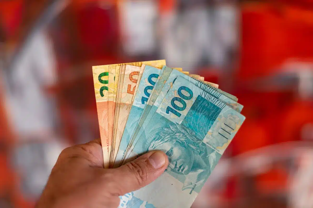 Pessoa segurando cédulas de dinheiro brasileiro com notas de 20, 50 e 100 reais.
