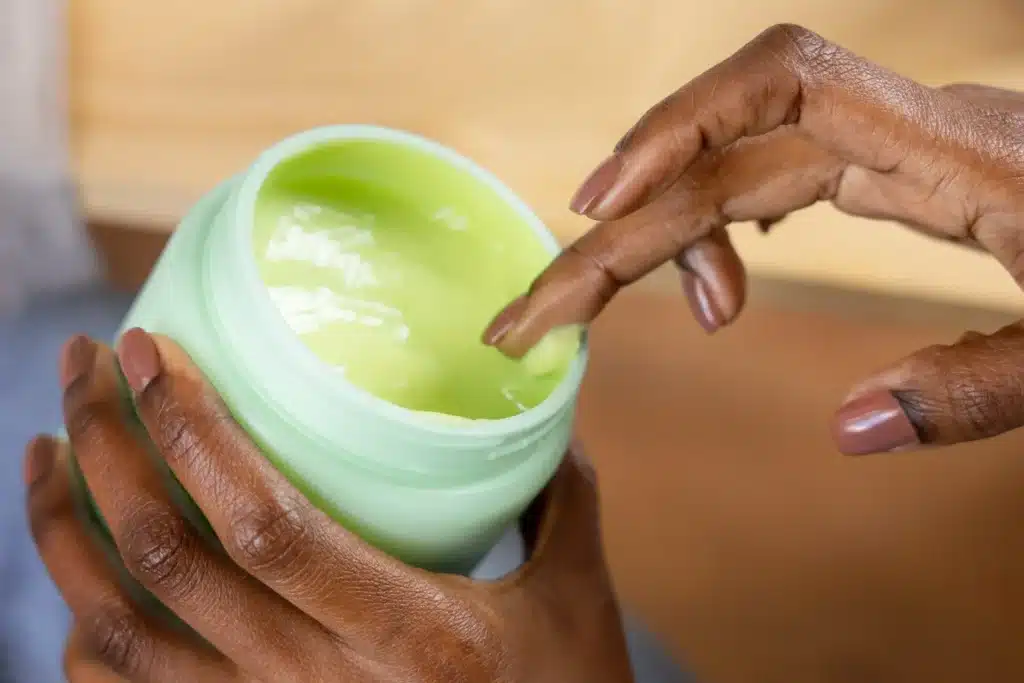 Mãos segurando pote com creme nutritivo à base de óleos naturais para tratamento capilar.