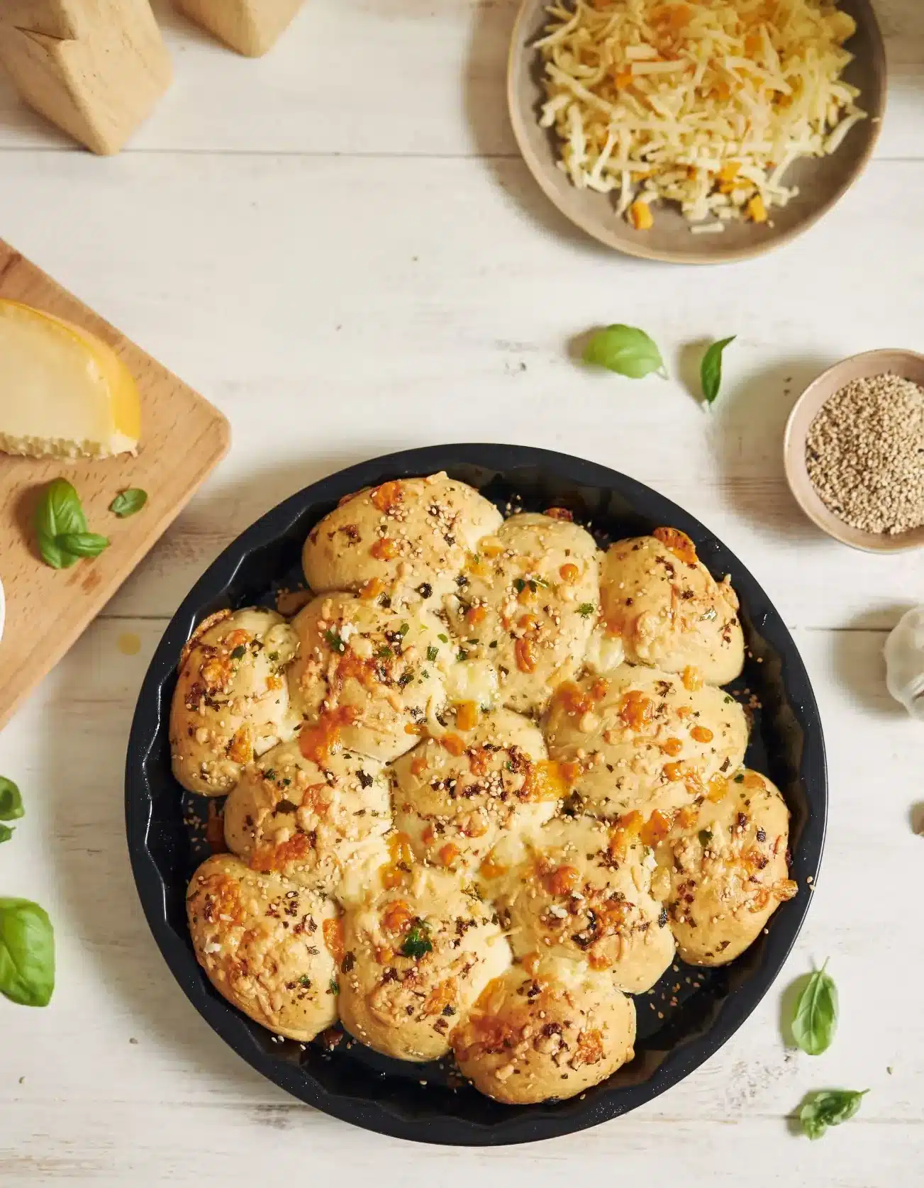 Pão de queijo com ervas assado em forma redonda, cercado por ingredientes frescos