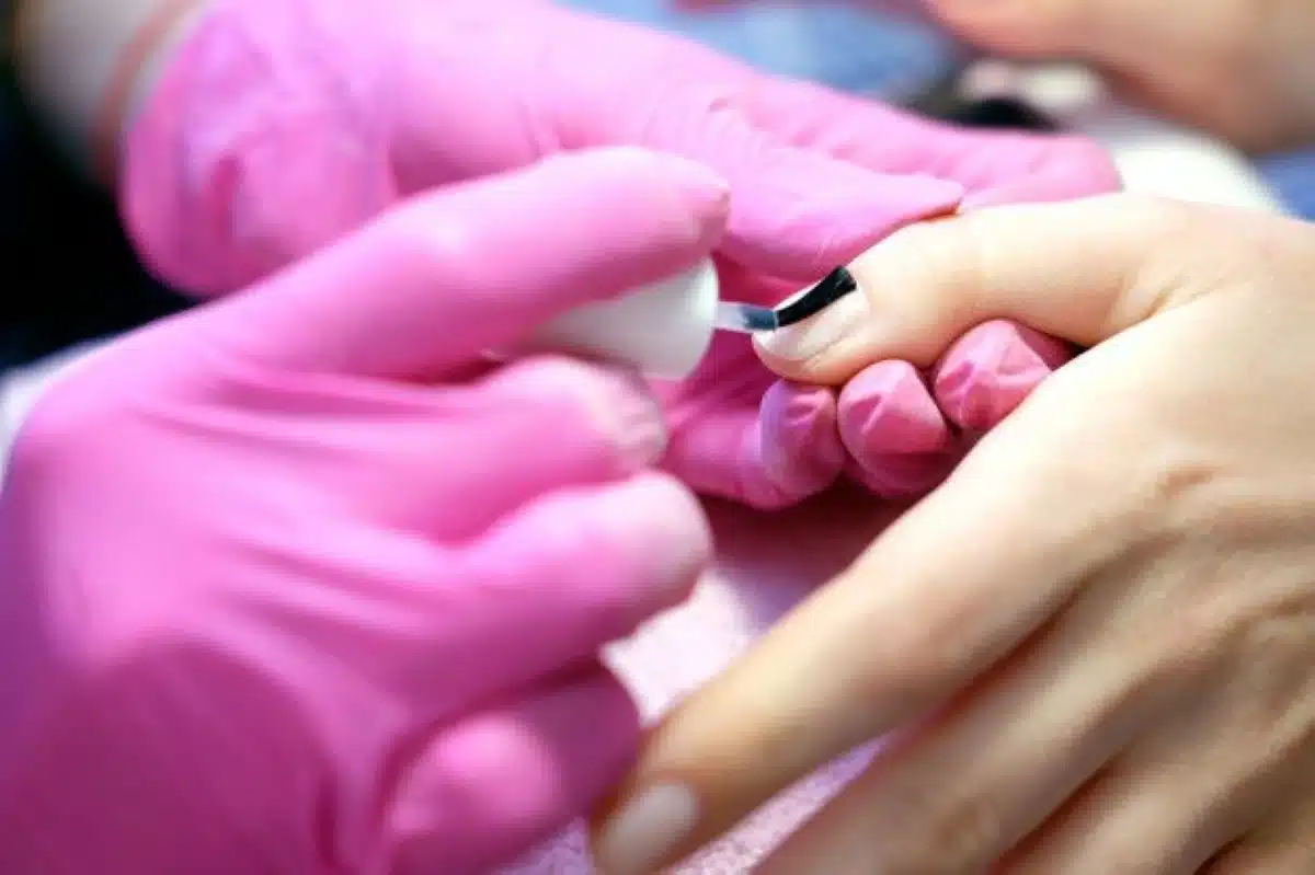 Aplicação de esmalte em gel em unha com profissional usando luvas rosas