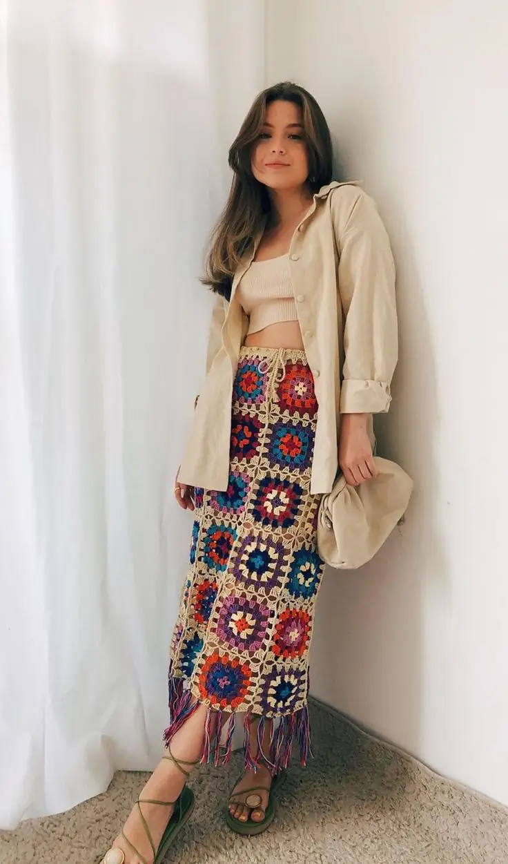 Mulher usando saia longa de crochê colorida com blusa básica e camisa aberta em look casual.