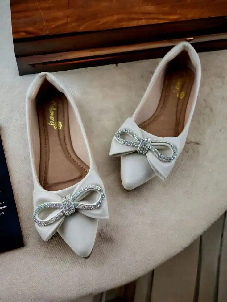 Sapatilhas femininas brancas com laços brilhantes e bico fino, combinando conforto e estilo moderno.