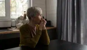 Mulher idosa pensativa olhando pela janela, refletindo sobre mudanças emocionais na terceira idade.
