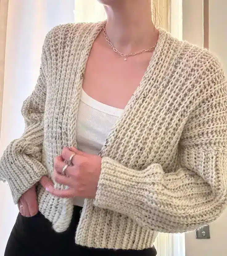 Cardigan de crochê bege usado sobre blusa branca, criando sobreposição moderna e casual.