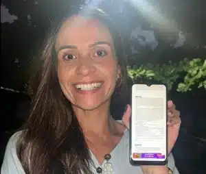 Taize dos Santos comemora a assinatura do primeiro contrato do Minha Casa, Minha Vida Classe Média segurando o celular com o documento exibido na tela.