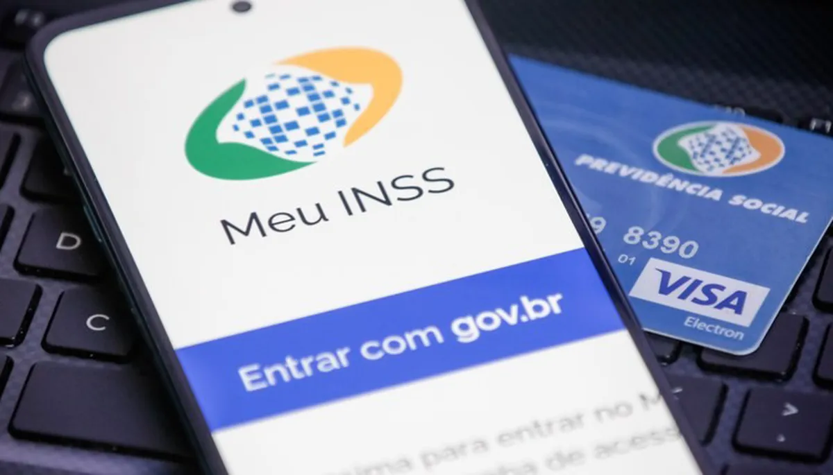 Aplicativo Meu INSS aberto no celular com cartão da Previdência Social ao fundo.