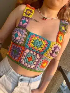Top de crochê colorido feito com quadrados vibrantes, usado com calça branca.