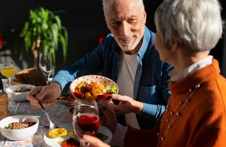 Idosos compartilhando uma refeição em um momento de alegria e bem-estar.