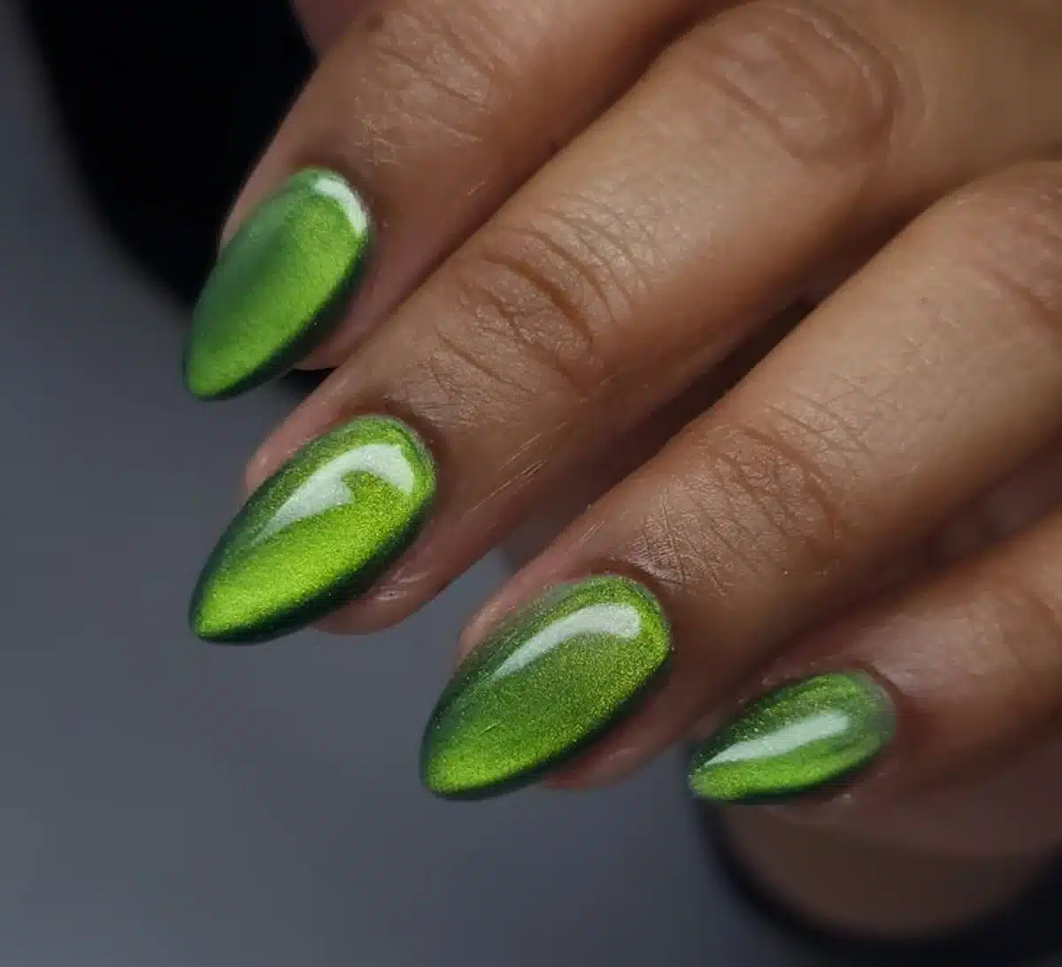 Unhas decoradas com efeito cat eye verde e acabamento brilhante.
