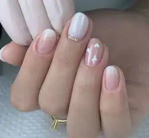 Unhas|, curtas com formato amendoadas, esmalte nude com detalhes delicados em branco e pequenos strass.