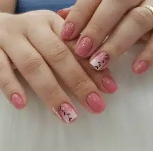 Unhas curtas com esmalte rosa e detalhes delicados de carimbo floral preto em fundo branco.