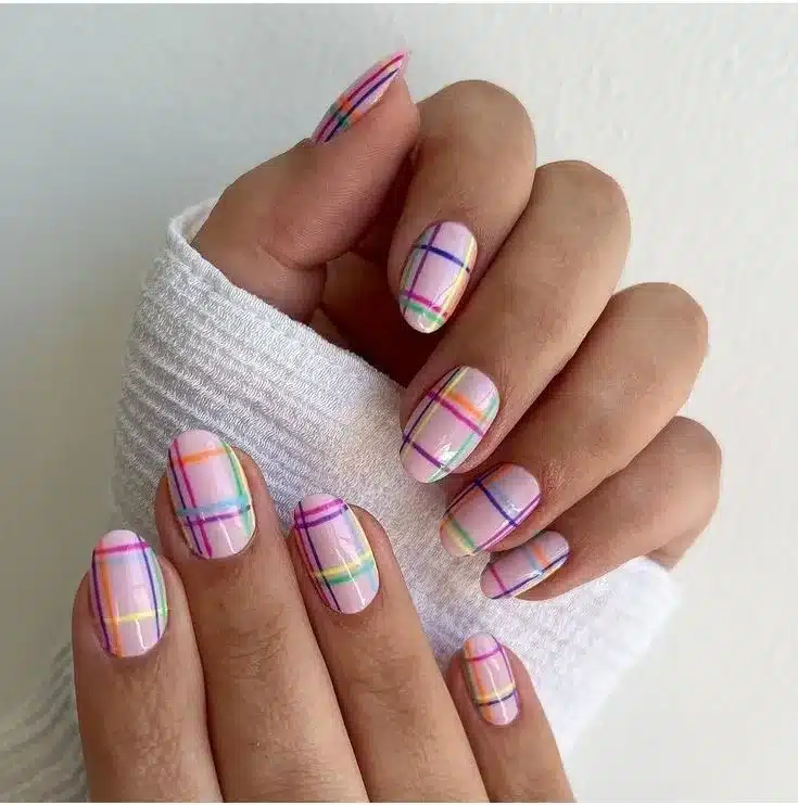 Unhas com fitas adesivas coloridas formando um padrão xadrez em fundo lilás