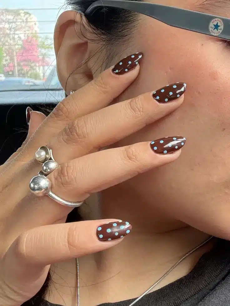 Unhas com esmalte marrom decoradas com bolinhas azuis em estilo poá