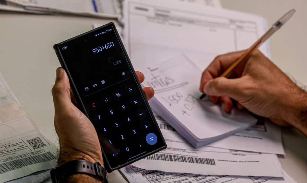 Pessoa calcula valores para quitar dívidas com ajuda de celular e anotações