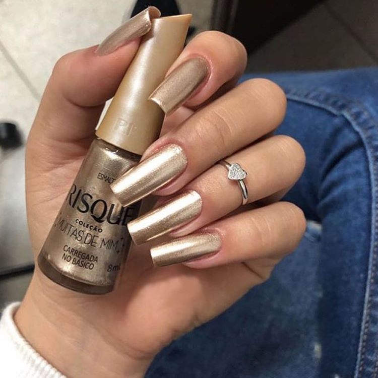 Mão segurando esmalte metálico Risqué com unhas pintadas na mesma cor dourada brilhante
