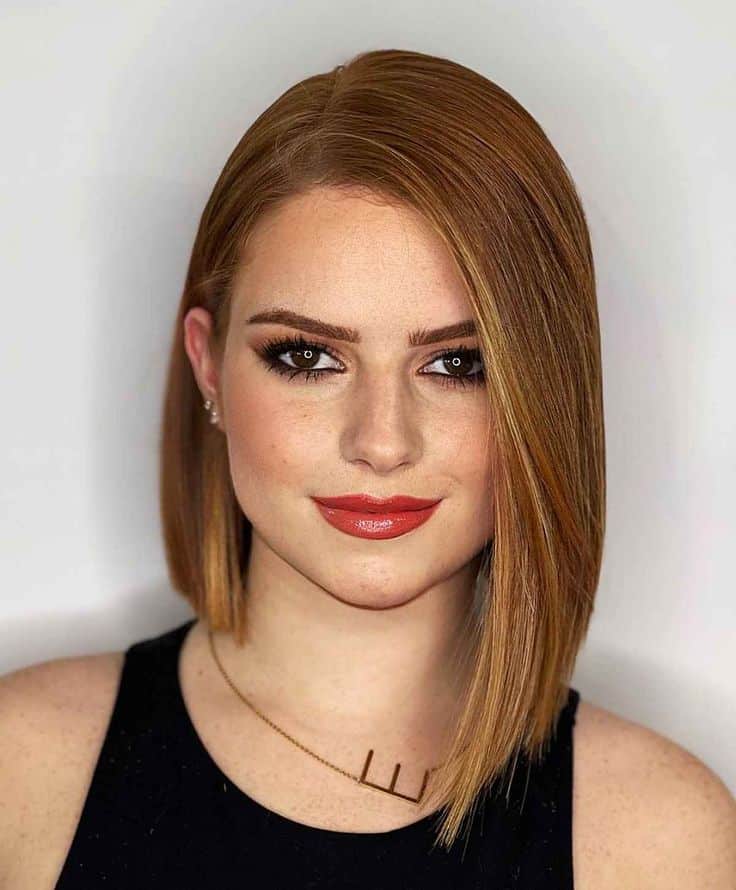Mulher com corte blunt bob assimétrico ruivo e acabamento liso com risca lateral