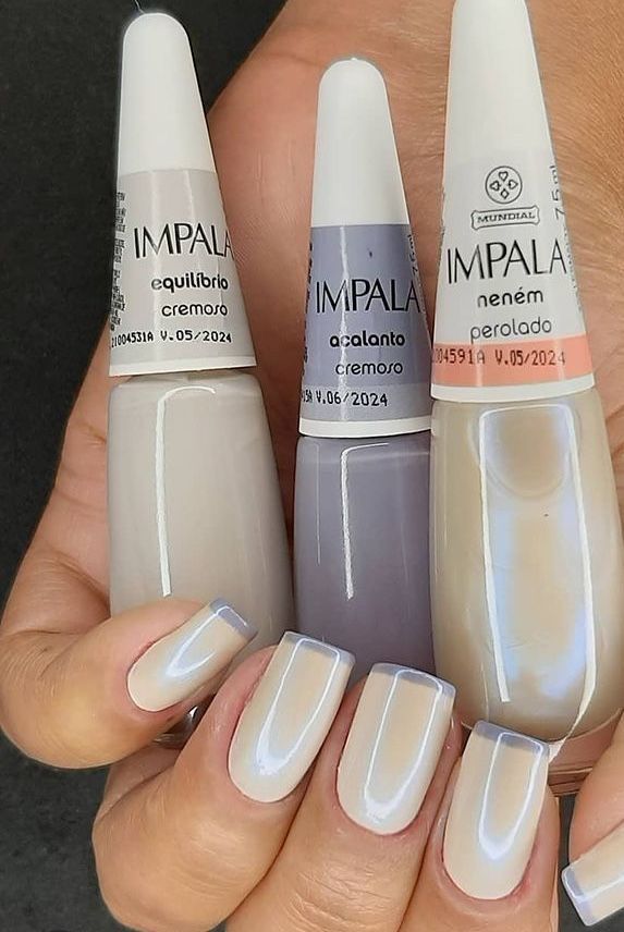 Mãos segurando três esmaltes Impala em tons perolados com unhas pintadas no mesmo estilo