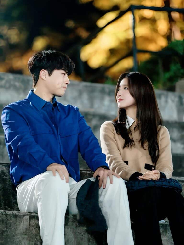 Cena romântica entre casal sentado em escadaria ao ar livre durante o dorama