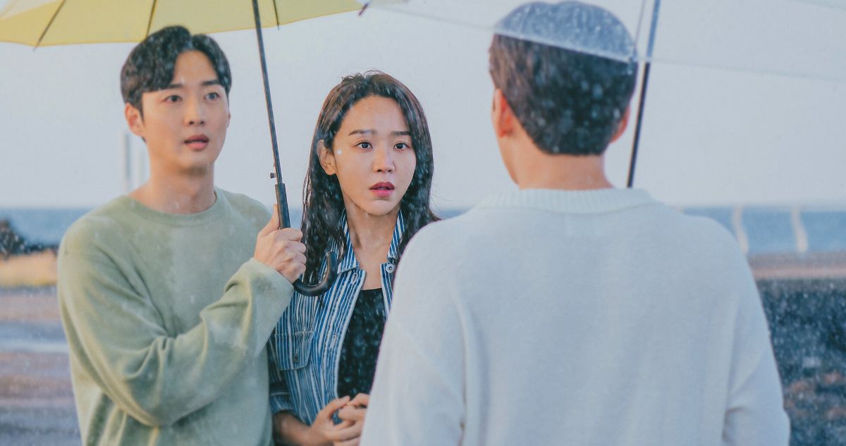 Cena do dorama De Volta às Raízes com casal debaixo de guarda-chuva encarando homem na chuva