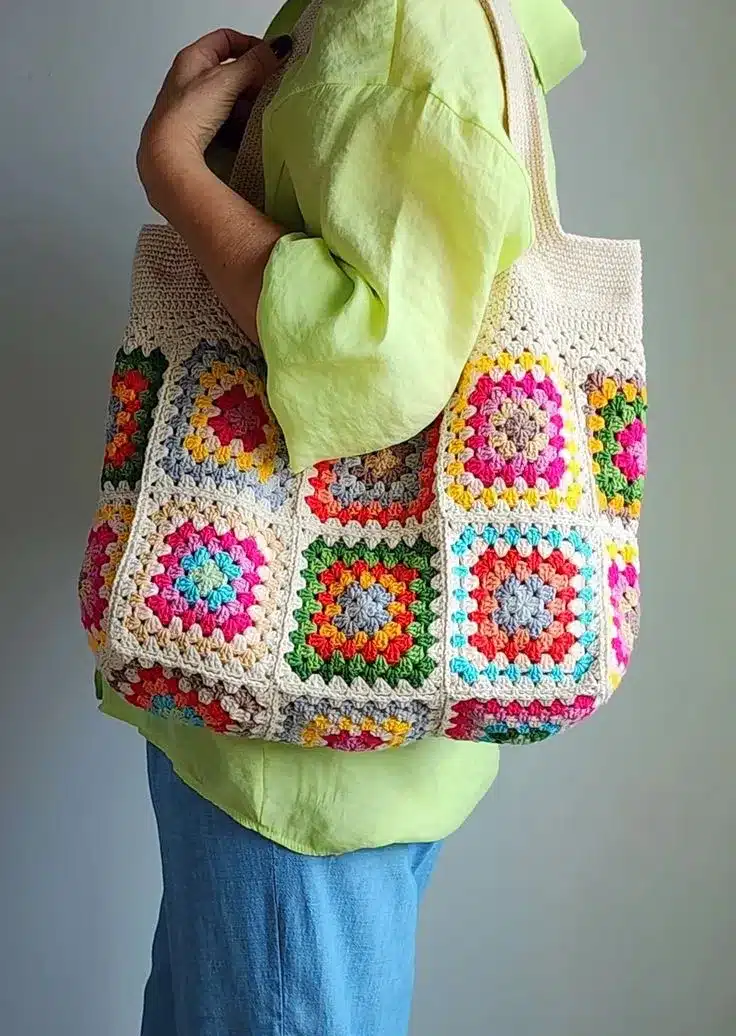 Bolsa de crochê feita com granny squares coloridos, com combinações de rosa, amarelo, azul e verde.