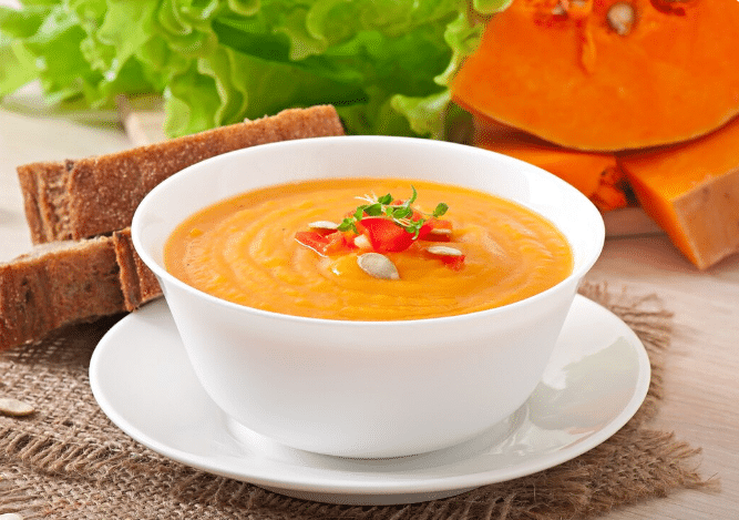 Caldo de abóbora cremoso, servido com pão e sementes de abóbora.