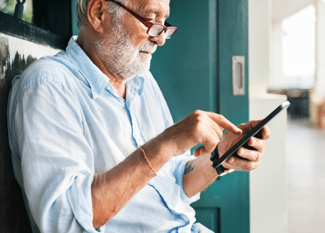 Idoso com óculos vermelhos usando um tablet com concentração