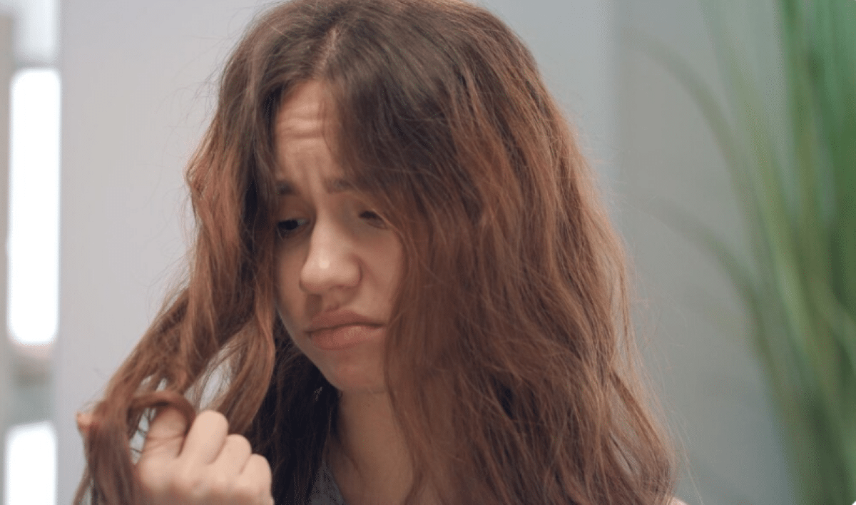 Mulher com cabelo ondulado e frizz, demonstrando insatisfação com os fios arrepiados.