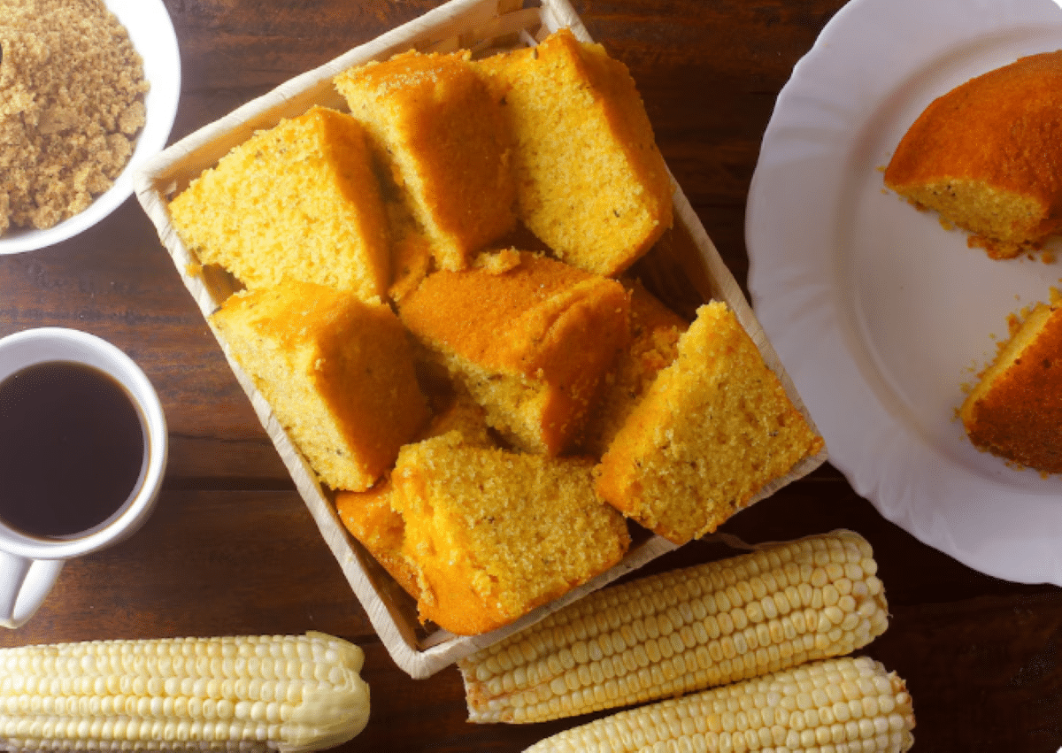 Fatias de bolo de fubá com goiabada servidas em cesta de palha, acompanhadas de café e espigas de milho