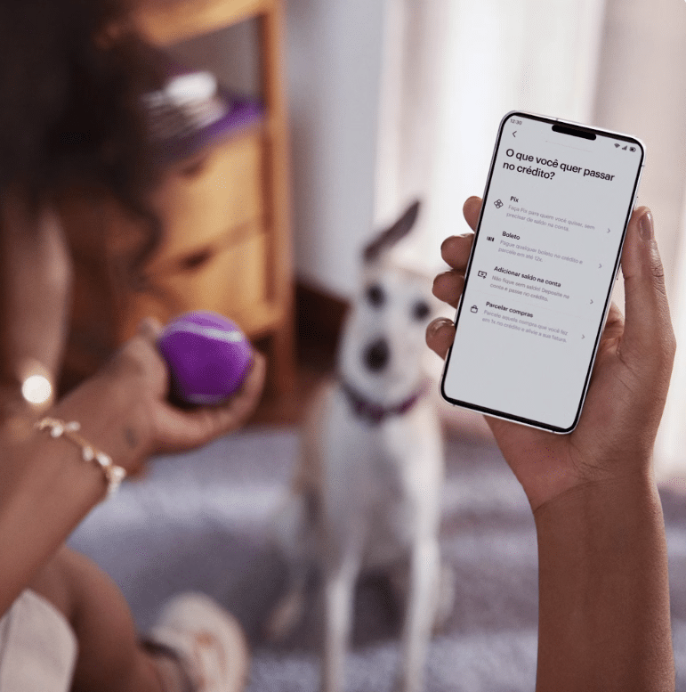 Pessoa utilizando o Pix por aproximação no aplicativo Nubank, enquanto segura uma bola de brinquedo e interage com o seu cachorro.