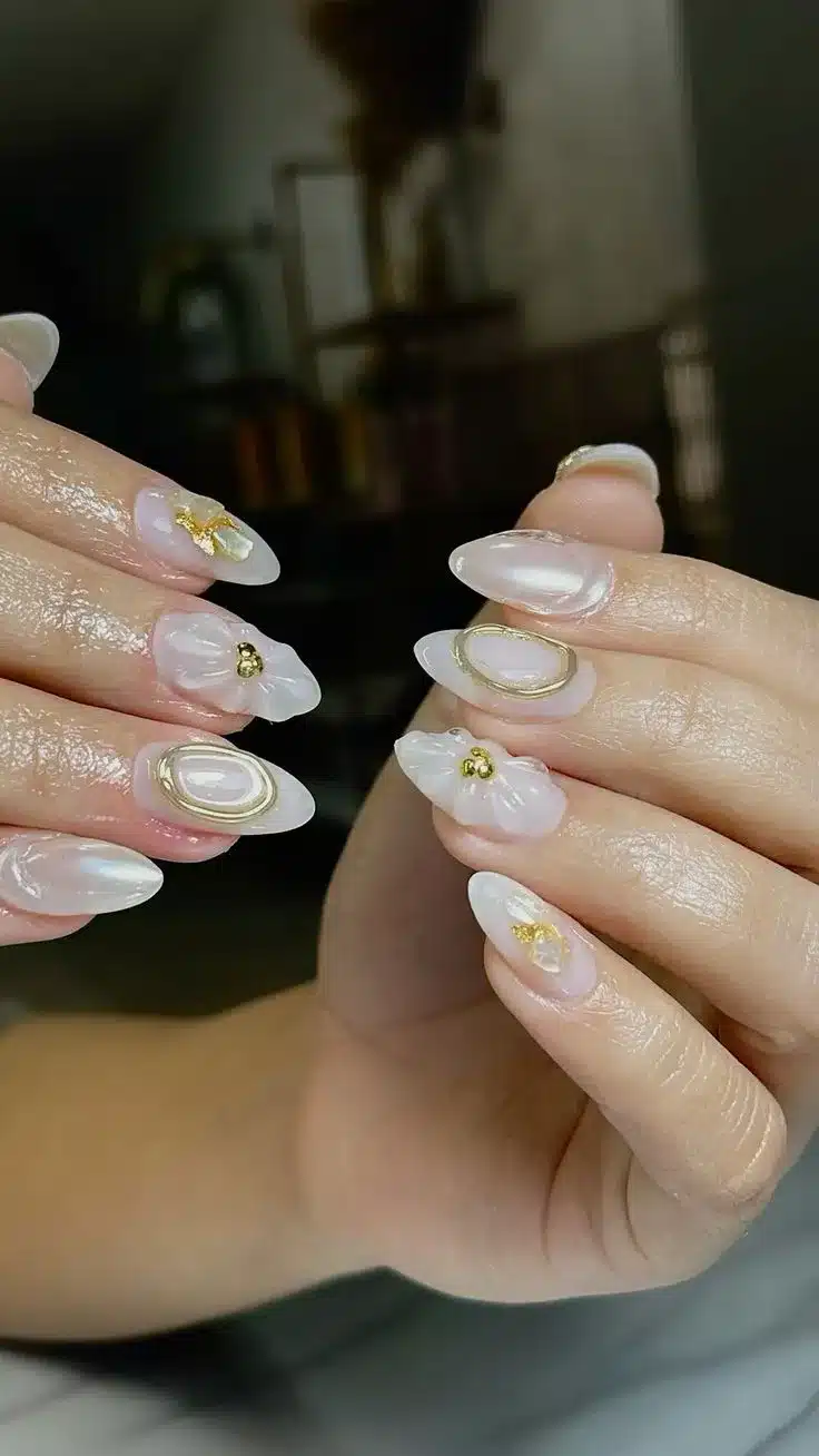 Design delicado de unhas com flores 3D e detalhes dourados.