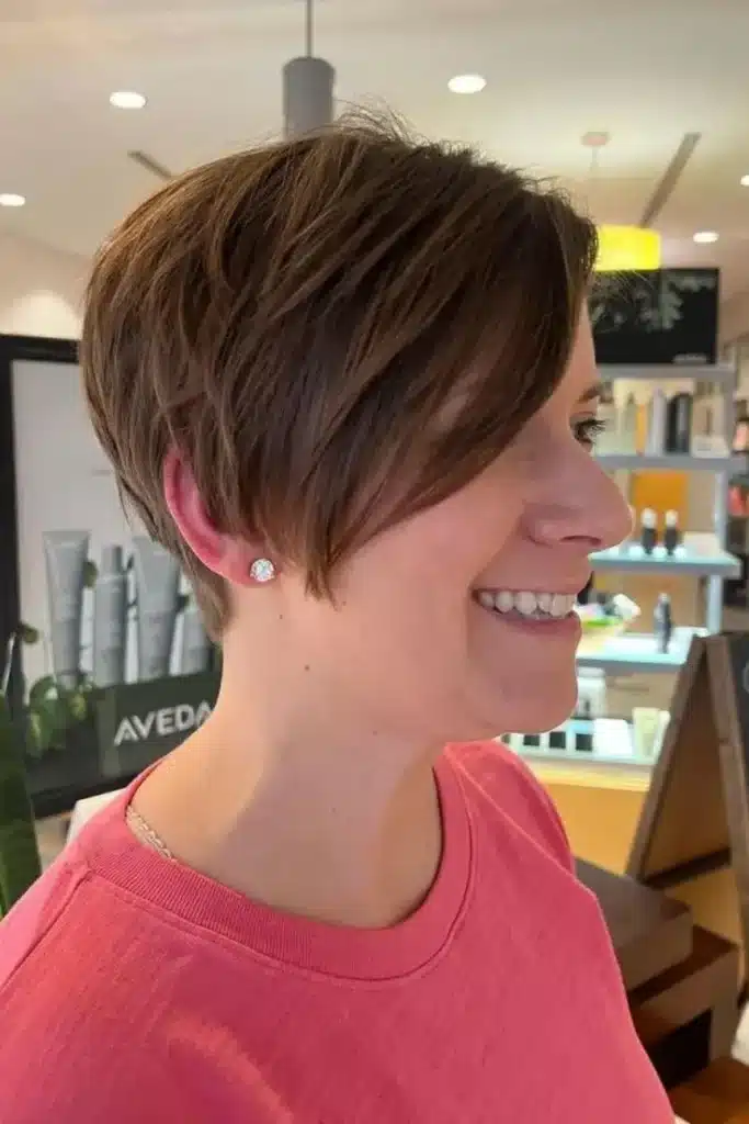 Mulher com corte de cabelo pixie clássico com franja lateral, sorrindo em um ambiente de salão
