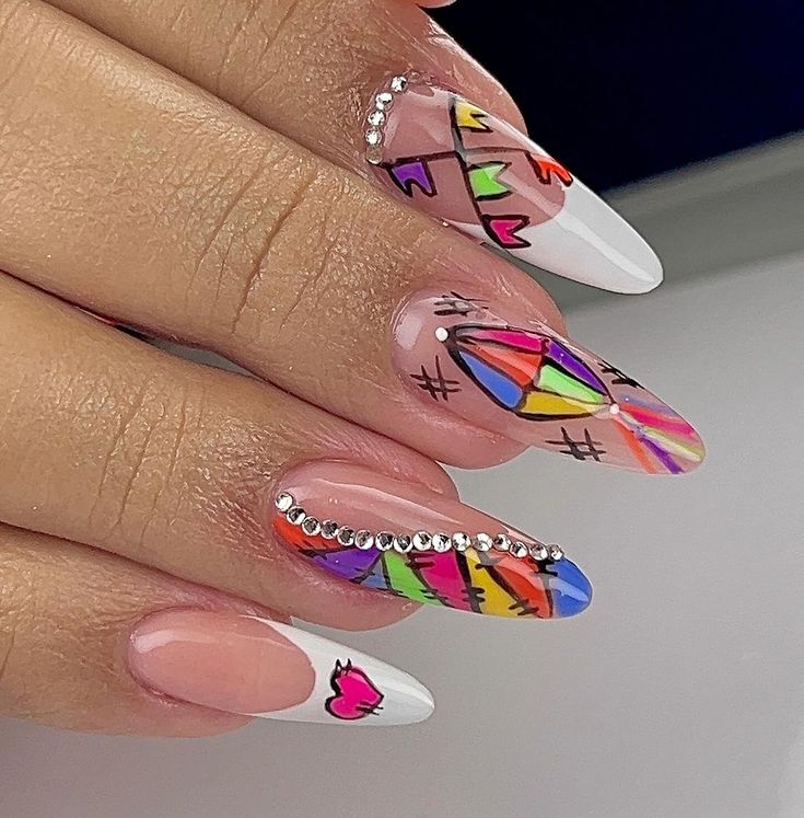 Unhas decoradas com desenhos coloridos e pedrinhas brilhantes, ideais para festas juninas.