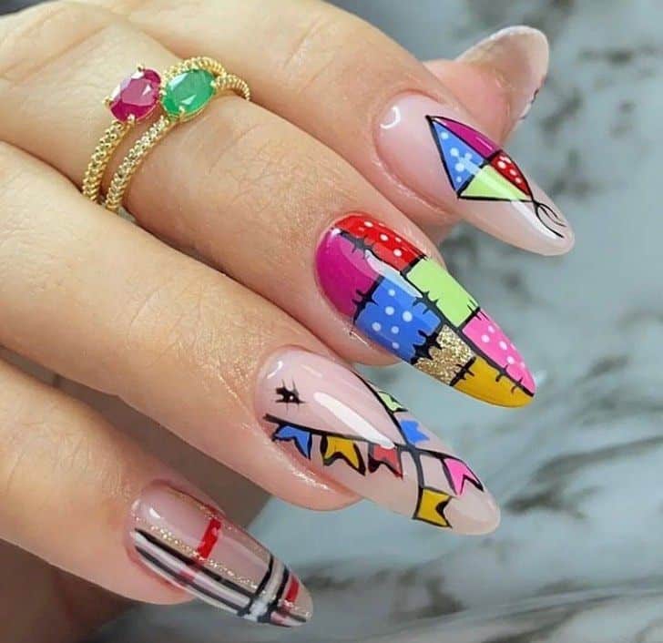Unhas de festa junina decoradas com retalhos de tecido coloridos e detalhes de bandeirinhas.
