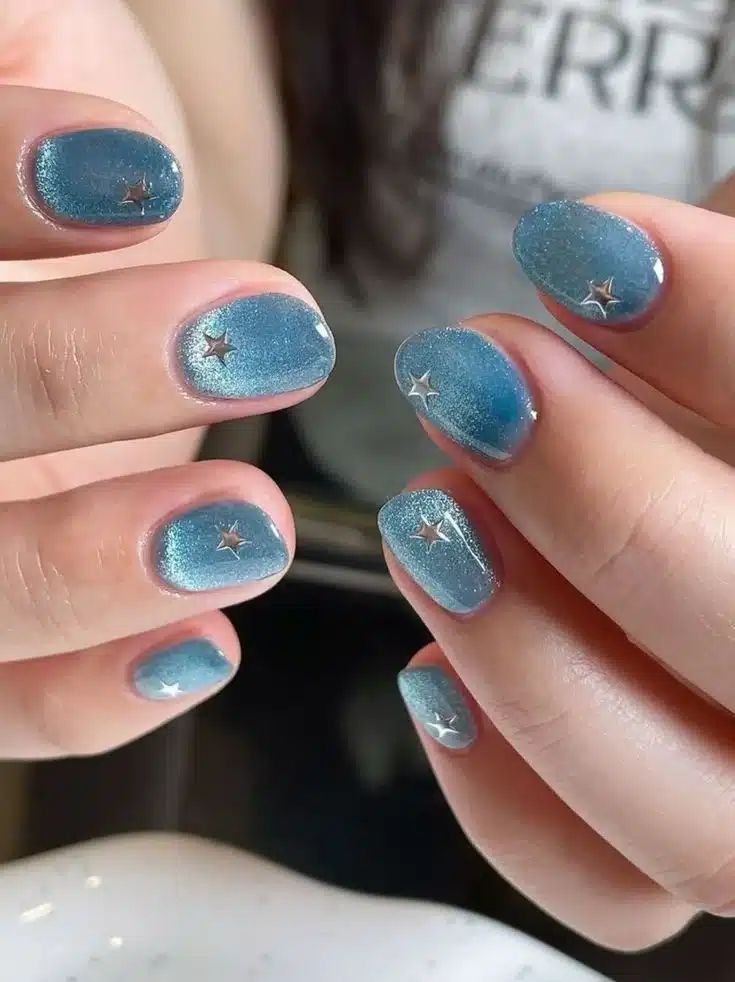 Unhas Jelly com acabamento transparente e brilho, adornadas com estrelas metálicas, representando a tendência das unhas coreanas.