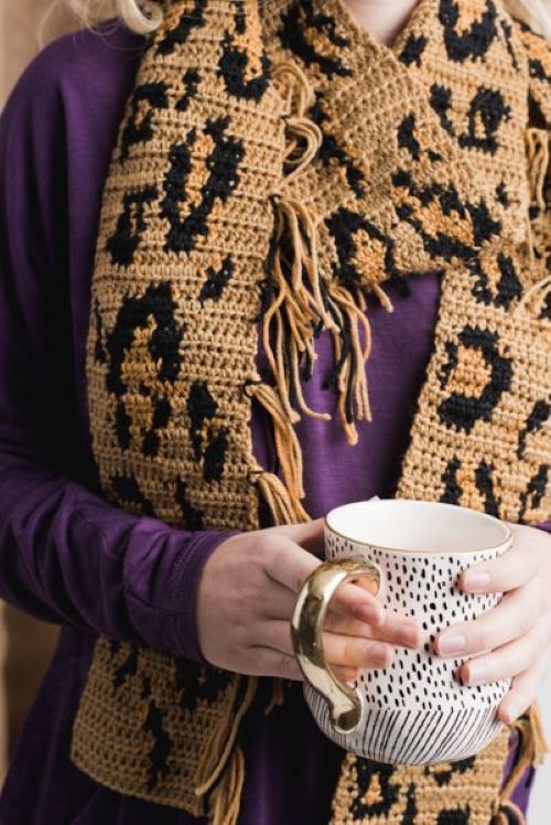 Cachecol de crochê com estampa de onça, nas cores marrom e preta, usado com uma blusa roxa.