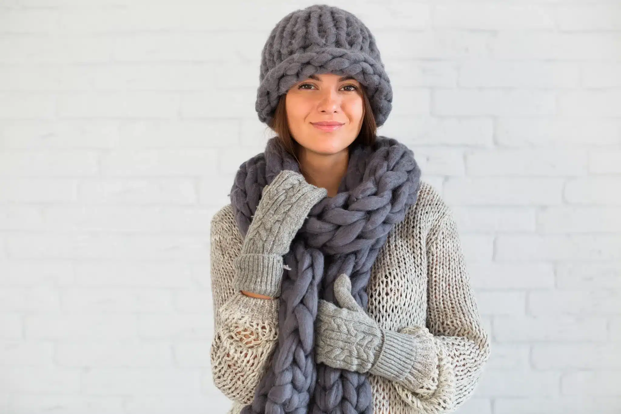 Mulher com cachecol grosso e luvas de crochê, utilizando acessórios de inverno em tons terrosos.