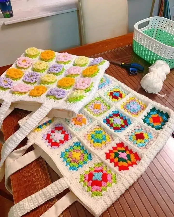 Bolsa de crochê com quadrados coloridos e flores em tons suaves, como rosa, lilás e amarelo, criando um visual delicado e alegre.
