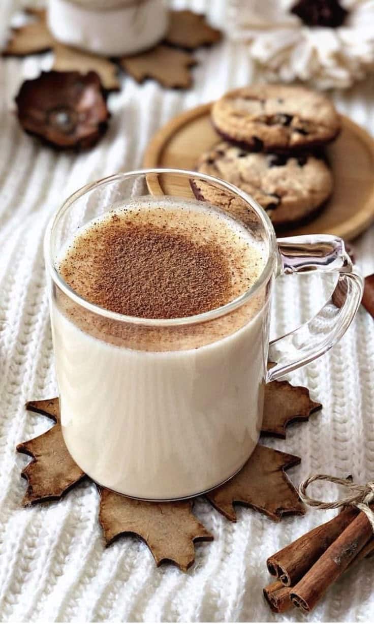 Bebida cremosa de inverno com canela servida em caneca de vidro ao lado de biscoitos