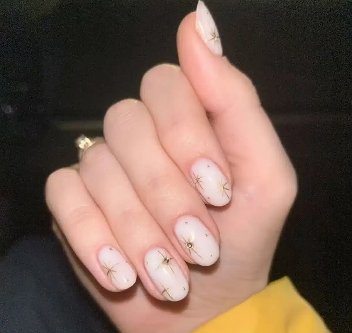 Unhas curtas e naturais com desenhos delicados e brilho dourado, estilo clean girl.