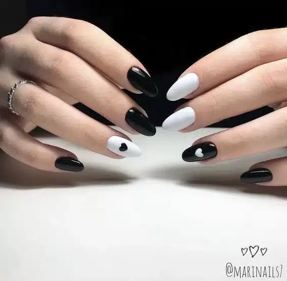 Unhas com cores preta e branca, decoradas com corações, representando a dualidade e emoções.