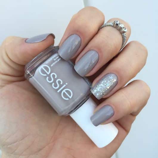 Unhas pintadas com esmalte cinza Essie, com uma unha decorada com glitter, combinando elegância e brilho.