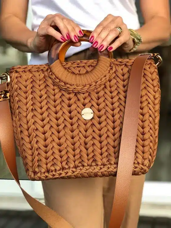 Bolsa de crochê marrom com alça de couro e detalhe circular em acrílico