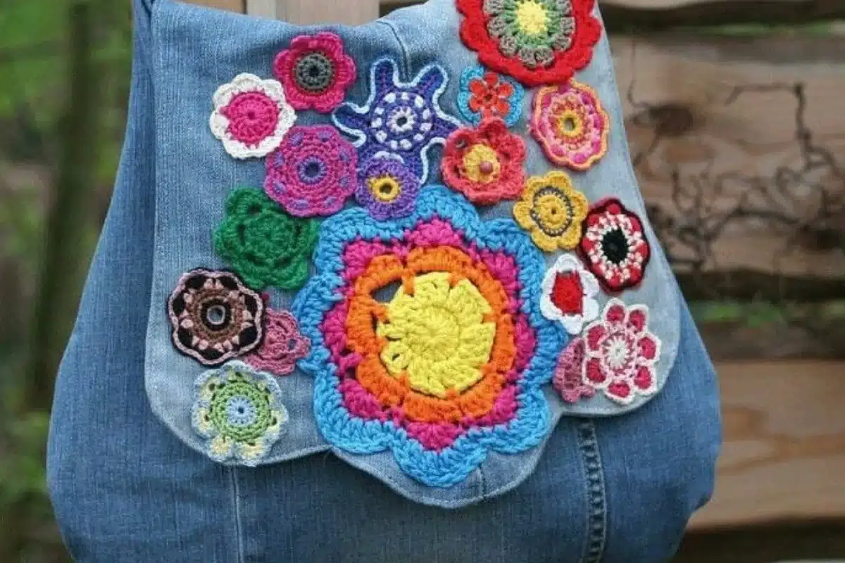 Bolsa jeans decorada com aplicações de flores de crochê coloridas.