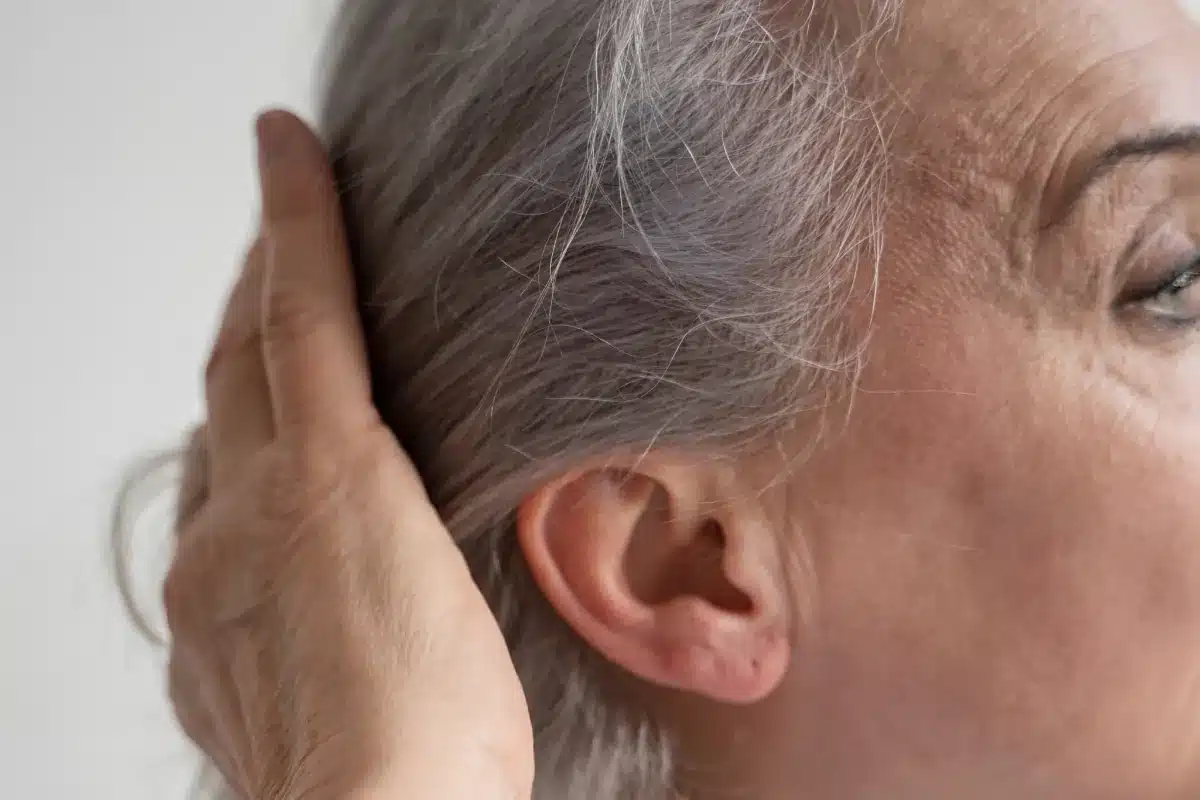 Mulher madura com cabelos grisalhos penteando os fios com a mão.
