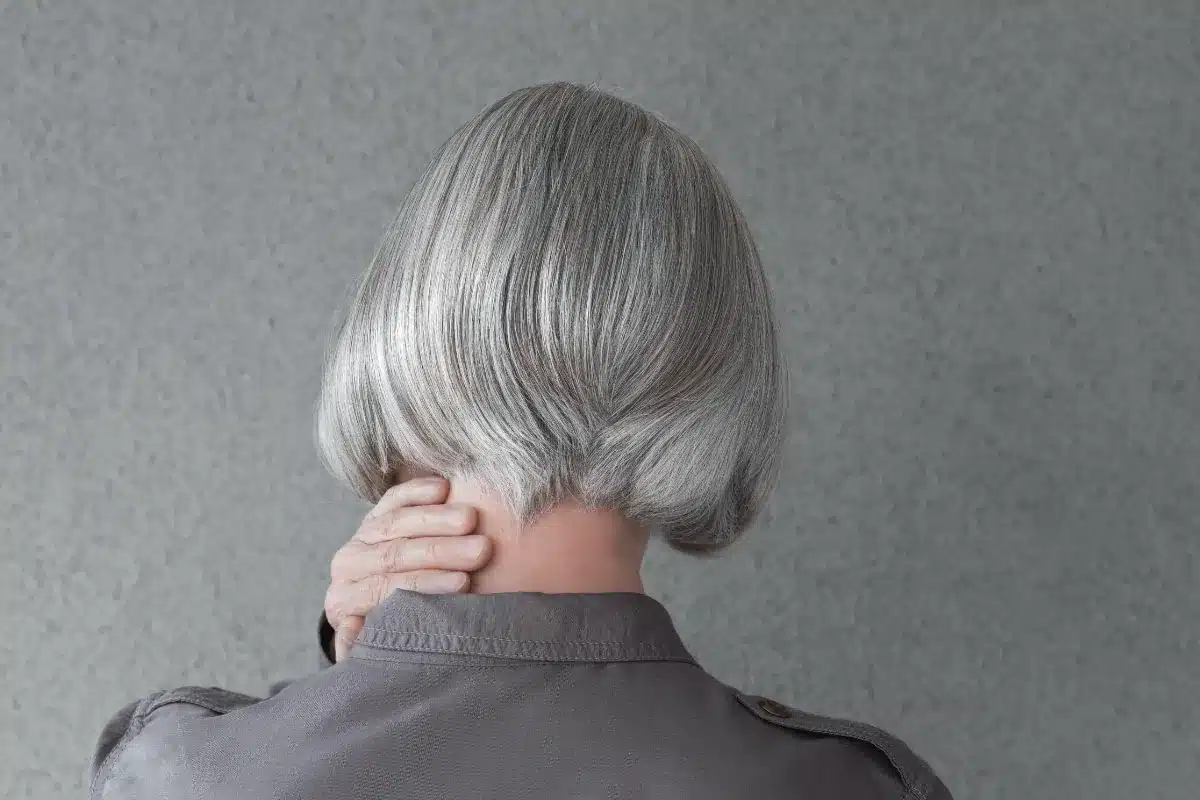Mulher com cabelo grisalho visto por trás, simbolizando maturidade e estilo natural.