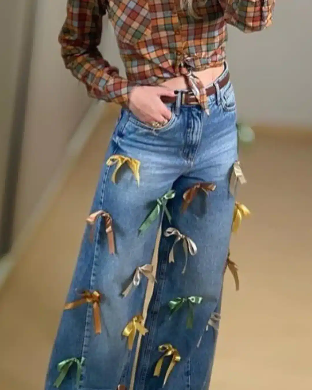  Calça jeans azul com laços coloridos costurados e camisa xadrez amarrada na cintura.